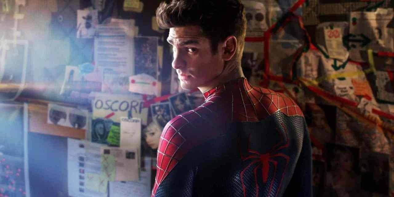 Andrew Garfield dressed in the Spider-Man suit looking behind him. The background is his bedroom with plans and images all over the wall