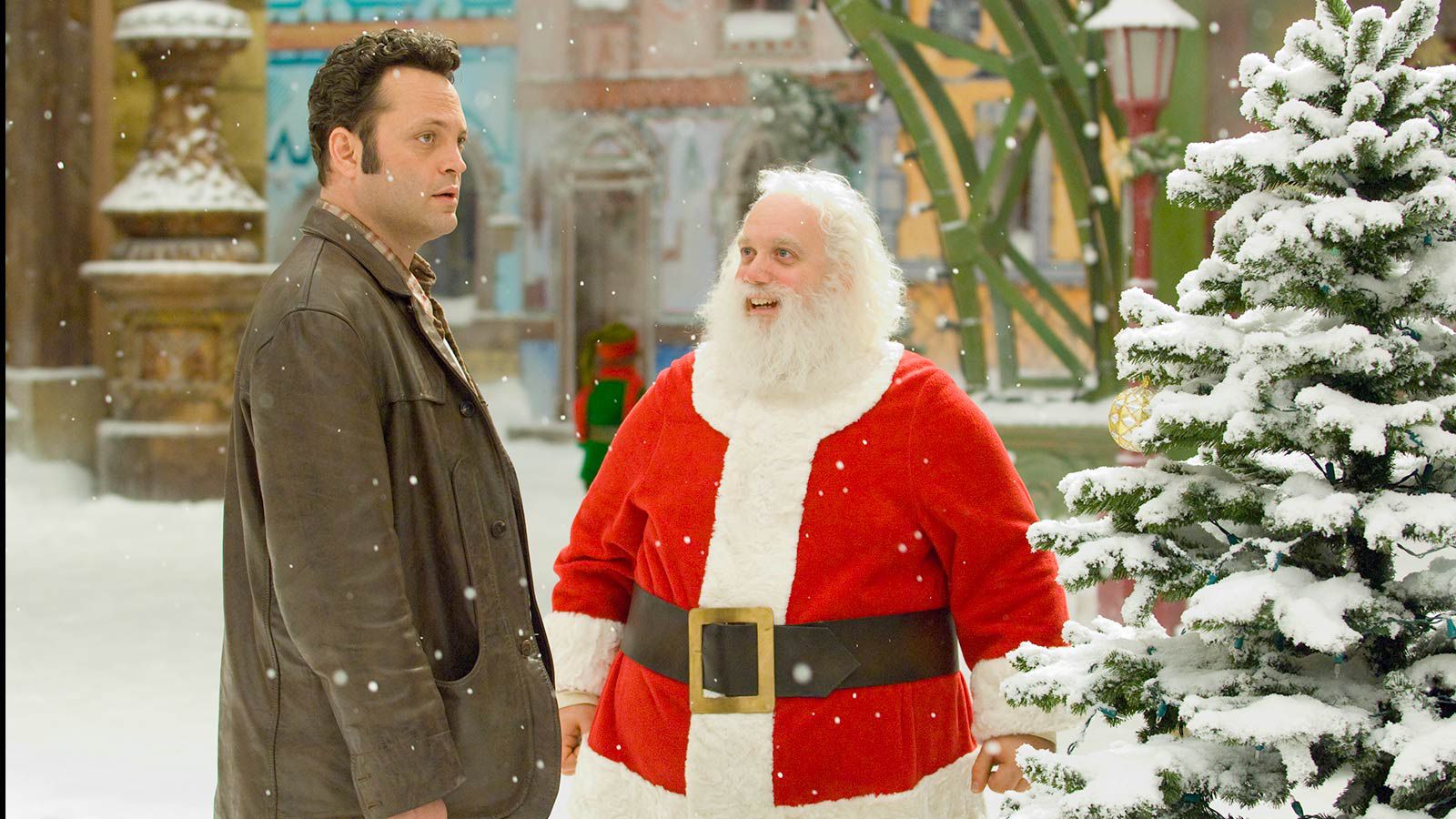 Vince Vaughn as Fred Claus and Paul Giamatti as Nick Claus. It's snowing in the scene, and there is a tree next to them at the North Pole.