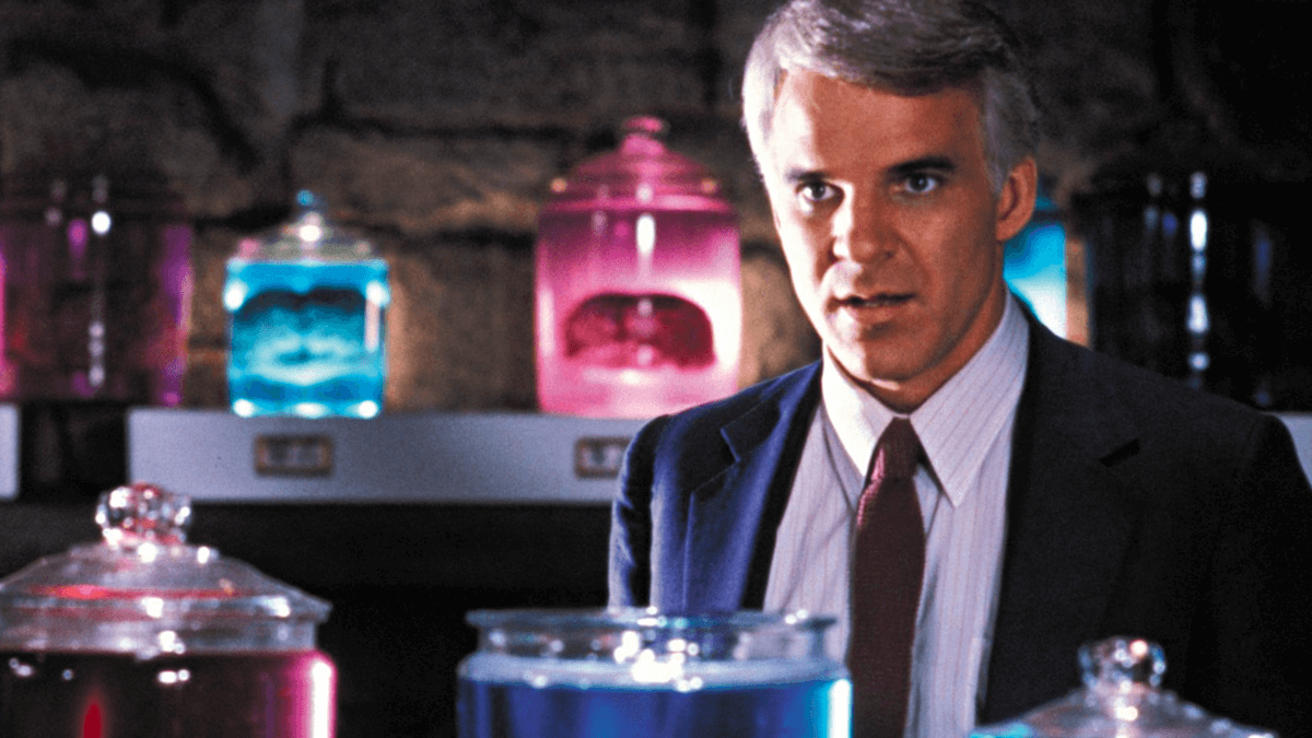 Actor, Steve Martin, wearing a suit as his character Michael, standing infront of jars of brains