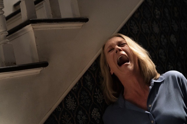 Jamie Lee Curtis as Laurie Strode screaming at the side of stairs in a house, in the movie Halloween Ends.