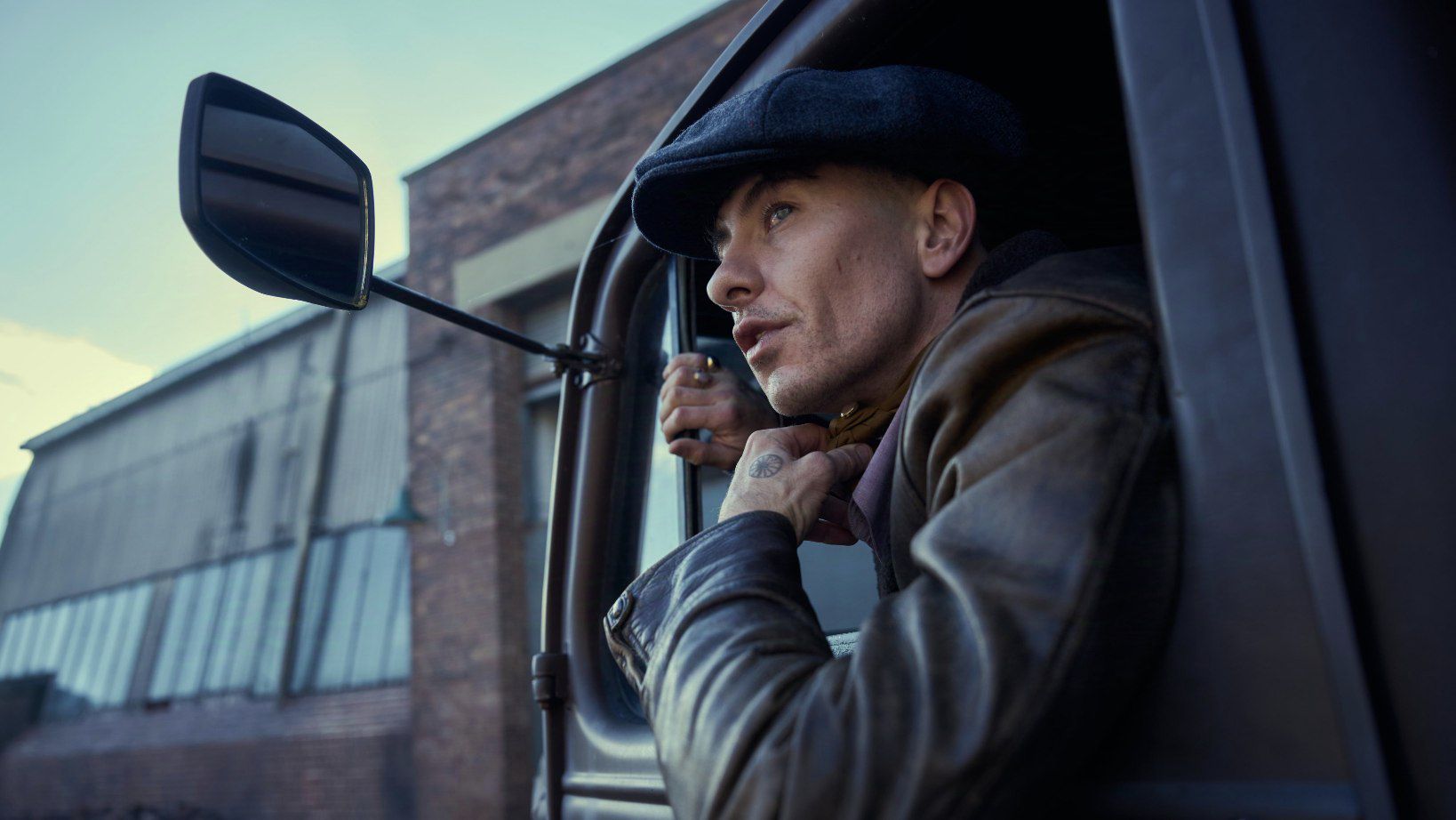 Barry Keoghan dressed in a black jacket and cap, sitting in a truck for Peaky Blinders film