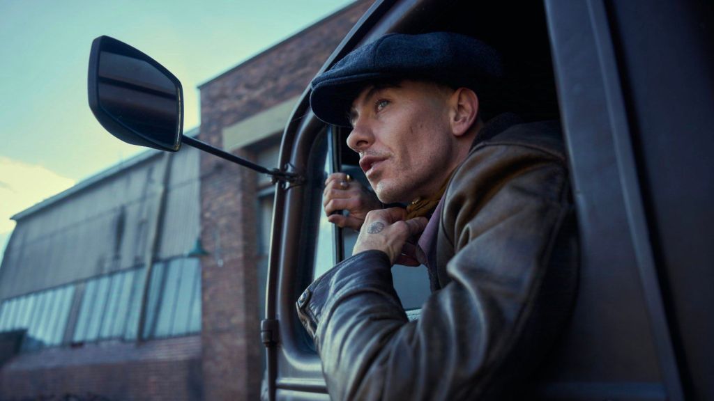 Barry Keoghan dressed in a black jacket and cap, sitting in a truck for Peaky Blinders film