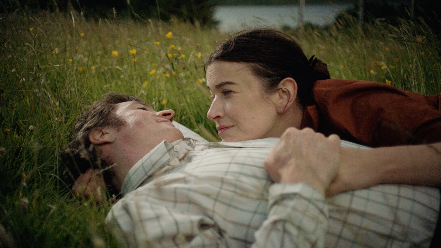 Man and woman laying closely on the grass smiling at each other