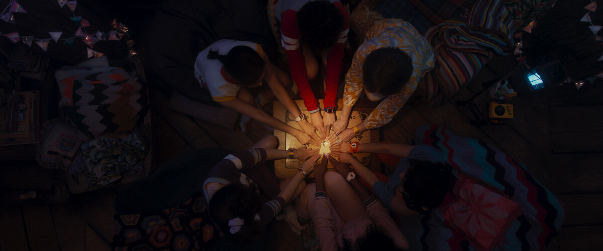 Agatha All Along scene where characters are gathering around with their hands on a Ouija Board.