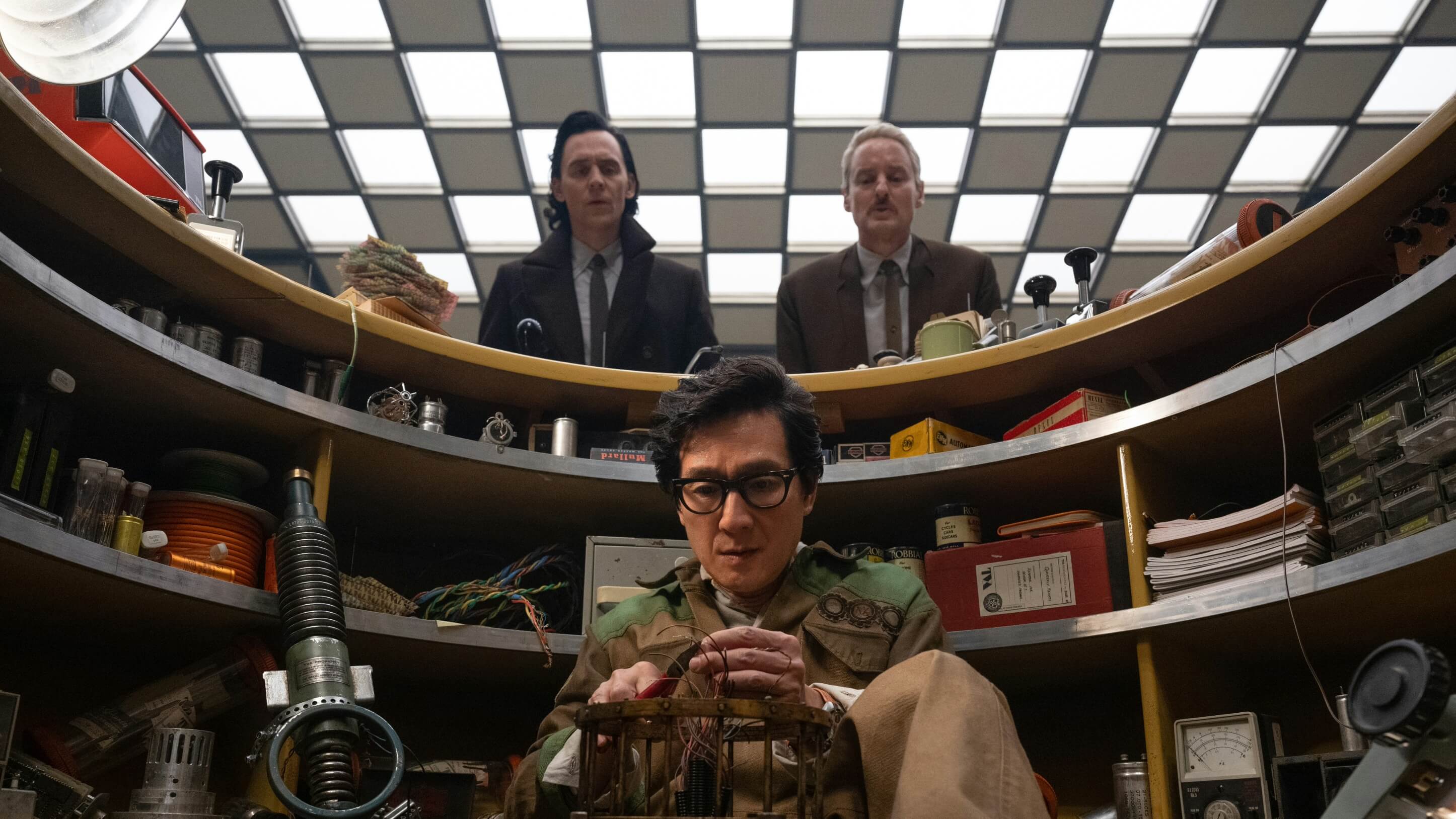 Ke Huy Quan as Ouroboros building something instrument in the TVA, with Loki and Mobius looking over a desk at him