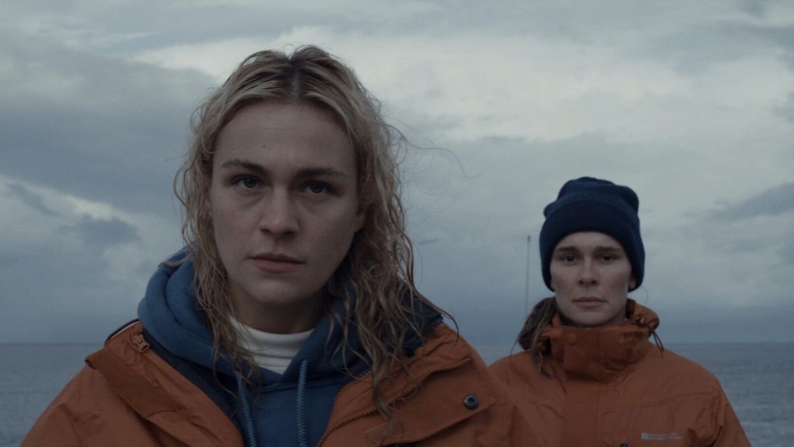 Two female characters from the movie Row, they both have orange waterproof jackets on