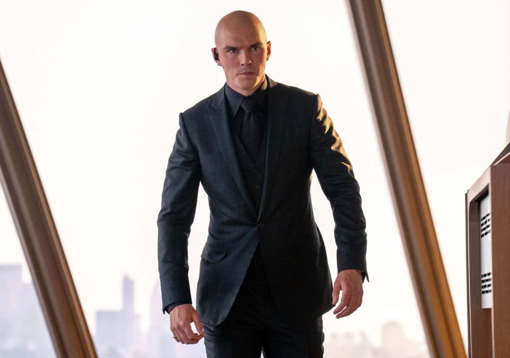 Lex Luthor is in his LuthorCorp building, dressed in a black suit, appearing to be focused on something.