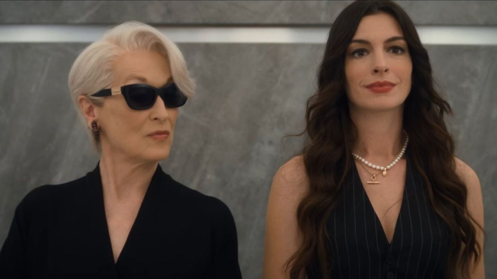 Two women (Meryl Streep and Anne Hathaway) in an elevator of a fashion building, one wearing sunglasses and one without.