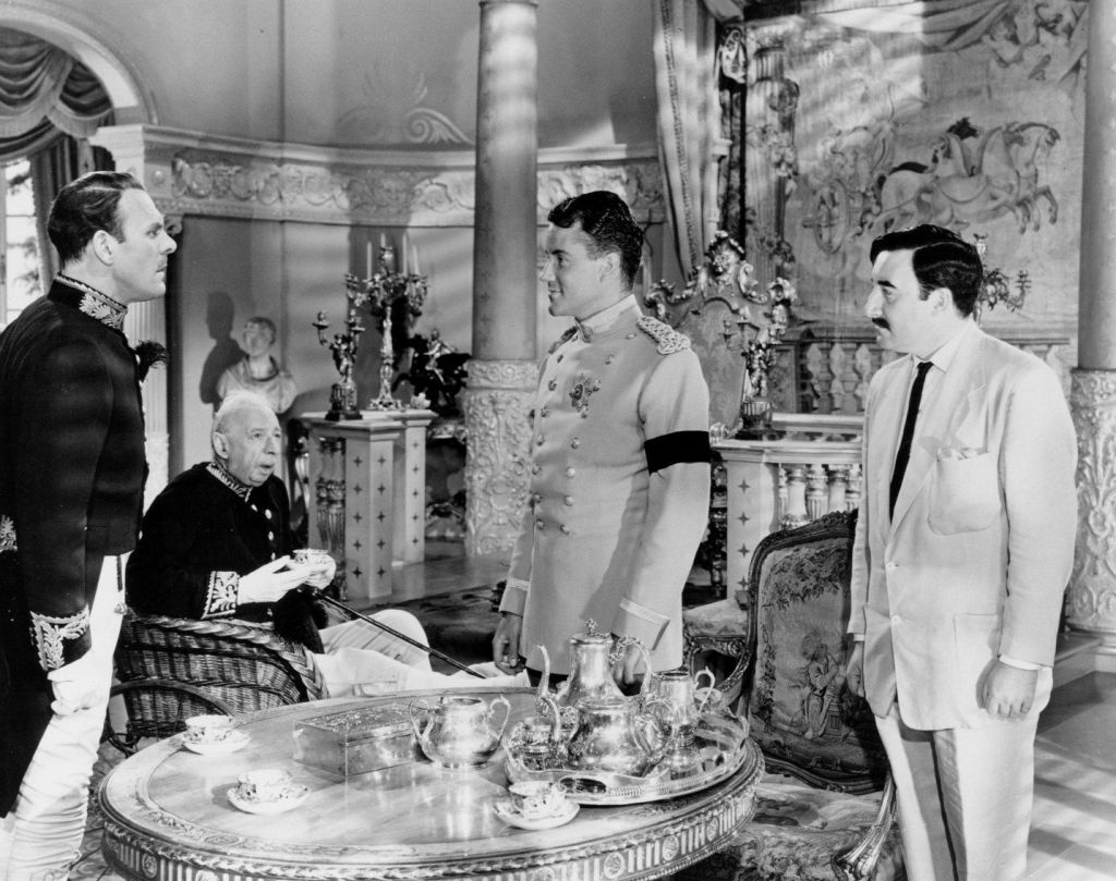 Peter Sellers and multiple other actors standing in a room dressed in suits and royal regalia.