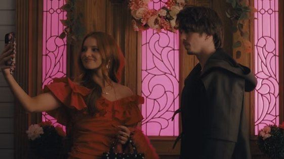 Charlize True and Seth Lee in 'Creepy AF', standing outside of an house entrance as they take a selfie.