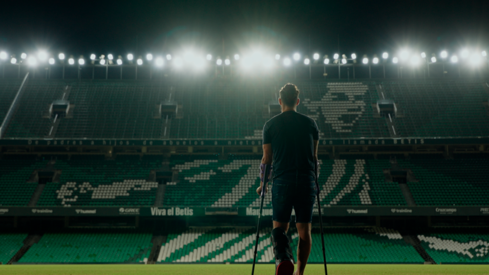 A man in crutches looking out to a football pitch